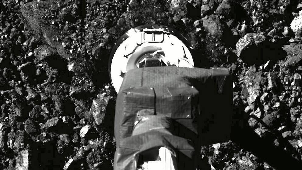 En svartvit bild på rymdsondens fot då den landat på asteroiden Bennu.