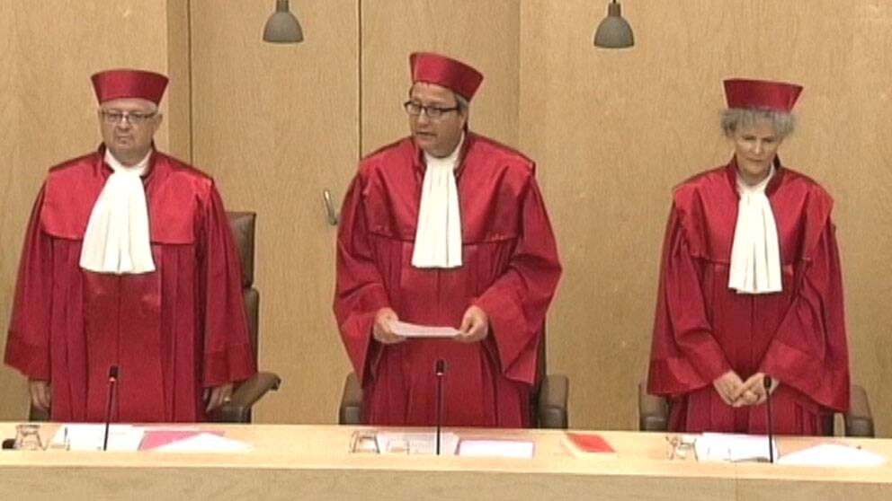 Tre rödklädda domare står upp varav en presenterar domen. Foto: Reuters.