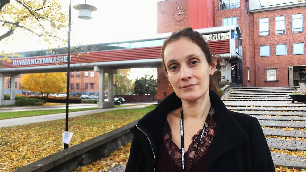 Biljana Sekaric står framför den långa trappan vid Rinmangymnasiets huvudentré. I bakgrunden syns även gångbron över vägen med texten ”Rinmangymnasiet” i stora gråa bokstäver.