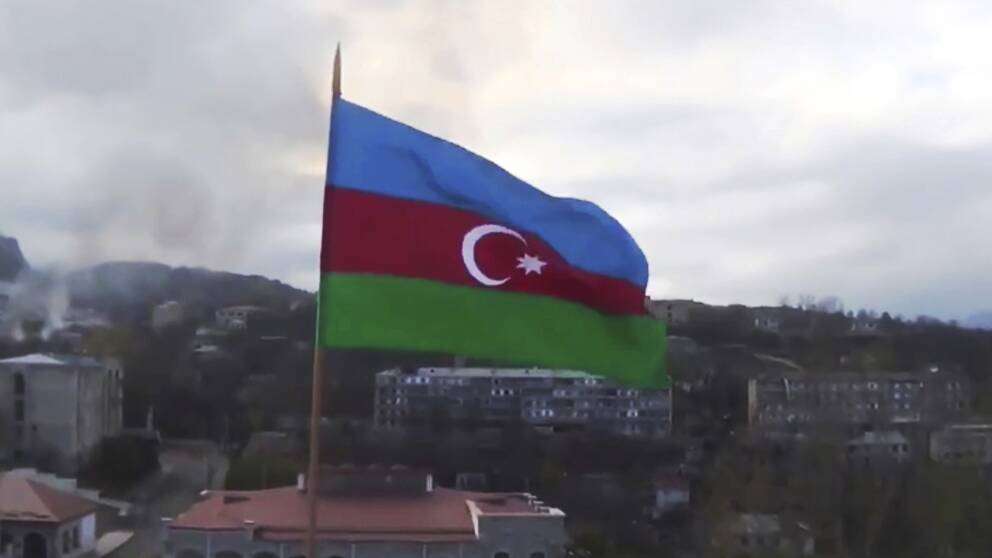 Azerbajdzjans flagga med staden Sjusji i bakgrunden, i den separatistiska regionen Nagorno-Karabakh. I bakgrunden syns även rök.