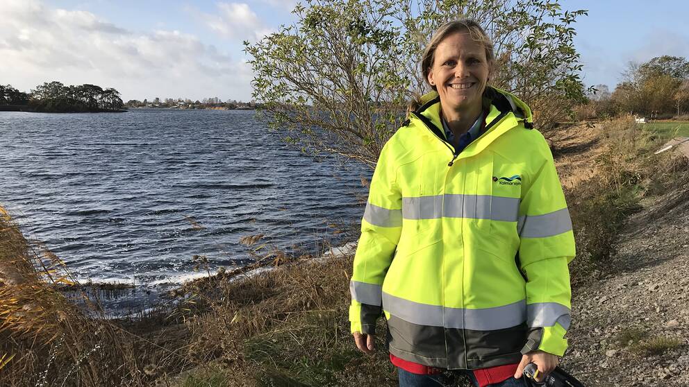 Kvinna i neongul jacka står framför öppet vatten.