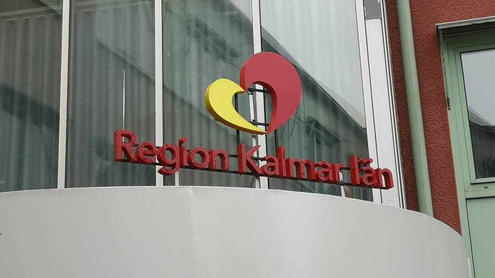 En bild på region Kalmar läns entréskylt utanför regionhuset. Det står Region Kalmar län med röda bokstäver och ovanför är deras logotyp. Ett hjärta i rött och gult.