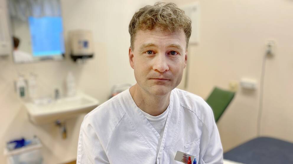Petter Ahrensted i vita läkarkläder sitter på en brits i ett undersökningsrum. 