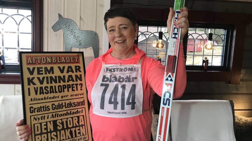 Medelålders kvinna som håller upp löpsida från aftonbladet och ett par skidor