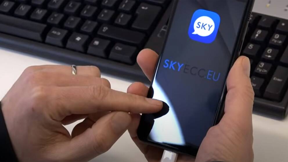 En polis sitter med en smartphone och öppnar appen Sky ECC.