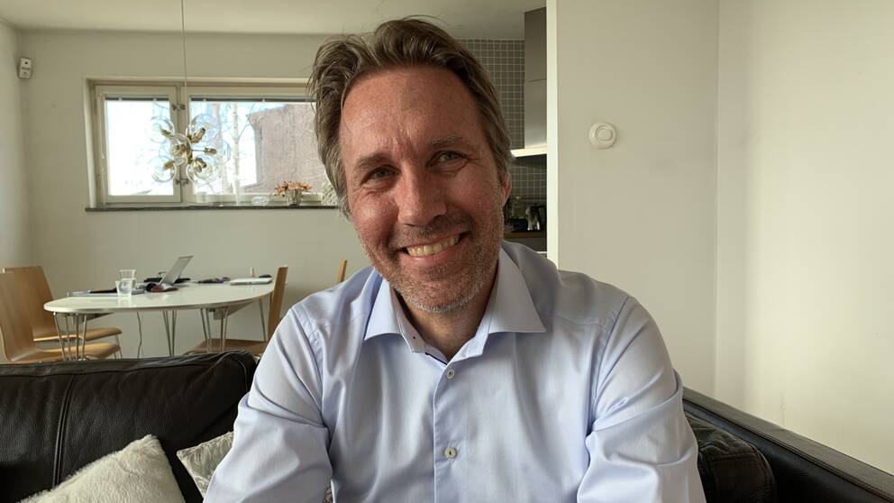 Peter Lundström ler mot kameran och sitter på sin soffa. Han har en blå skjorta.
