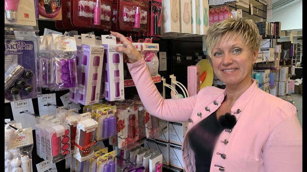 Sexleksaker på en vägg. Framför står en kvinna i rosa kavaj.