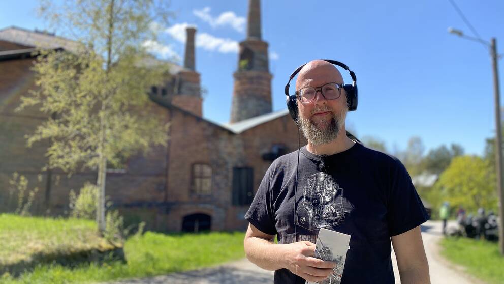 en man med hörlurar framför hyttan i Jädraås – en gammal tegelbyggnad med torn – solig sommardag