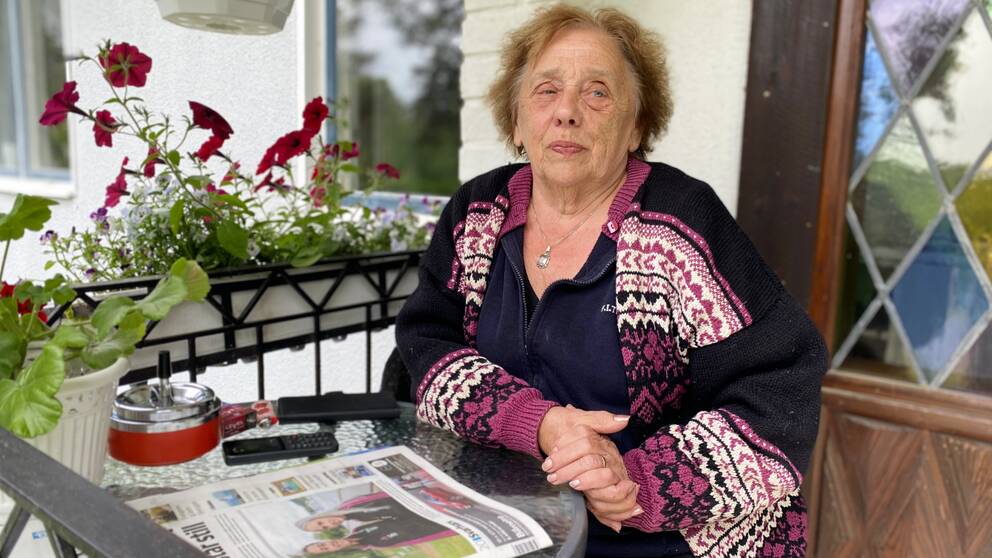 En äldre dam sitter på sin altan med en tidning framför sig efter att hon fått komma tillbaka sitt hem.