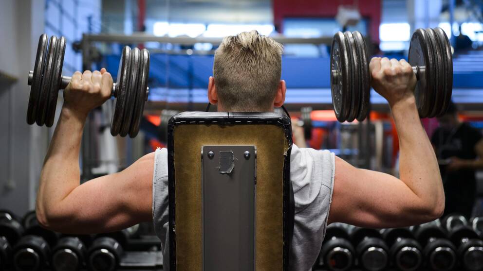 Ryggtavla på man som sitter och lyfter vikter på ett gym.