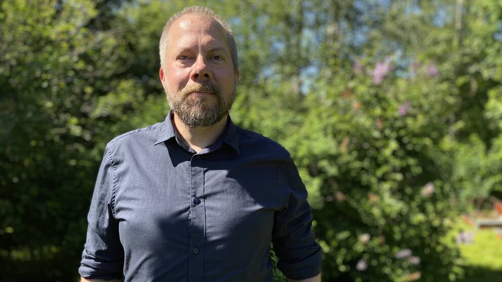 En man i skjorta står framför en grön buske.
