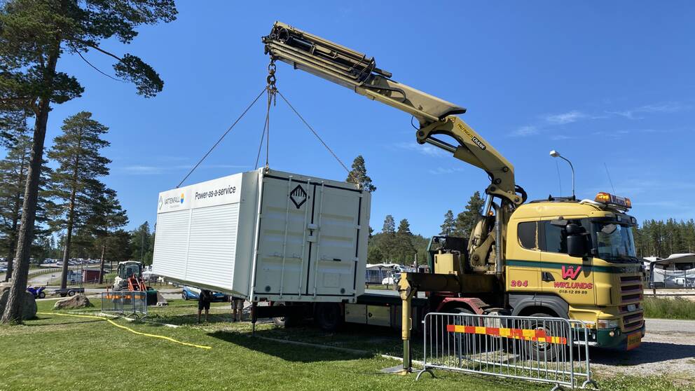 lastbild med kran lyfter en container ner på en gräsmatta