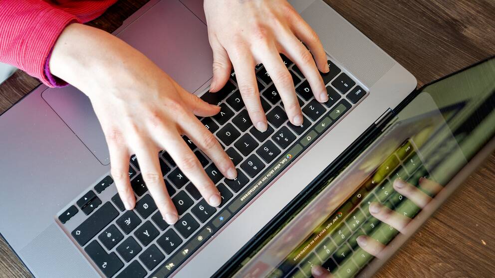Bilden är tagen uppifrån på två händer som skriver på en laptop.