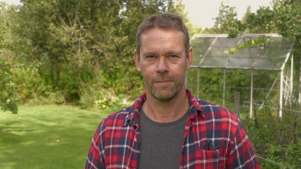 Mats Öfwerström i rutig skjorta framför grönska och ett växthus