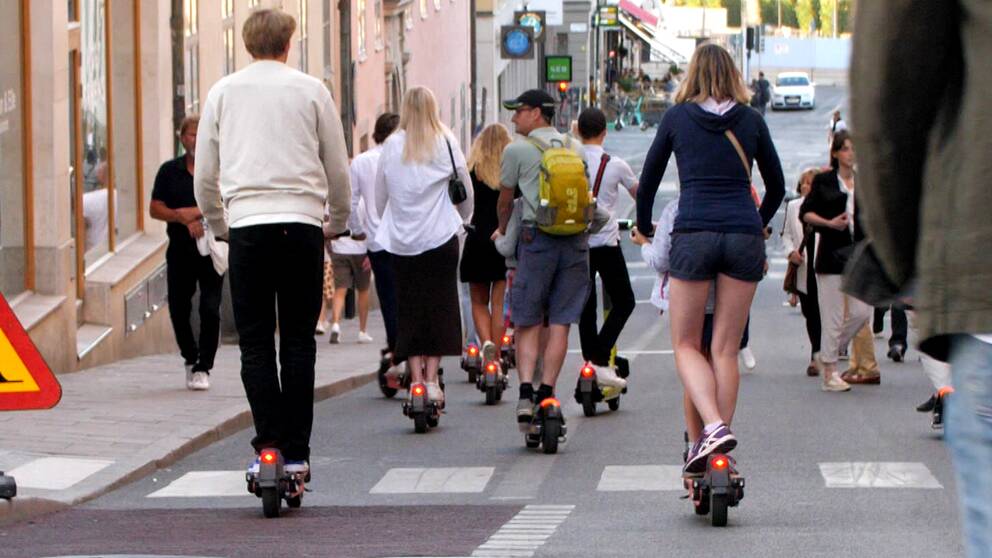 Flera personer åker elsparkcykel längs en gata.