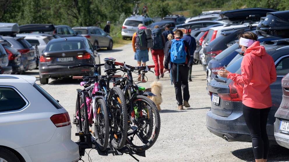 Bilar på en parkering. Cyklar och turister.