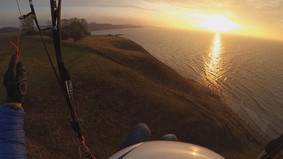 Bilden är tagen från en skärmflygningstur över Österlen. I bakgrunden går solen ner över havet.