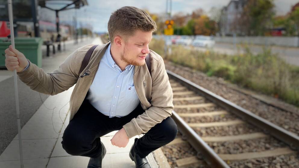 Mattias Winsa, i blå skjorta och beige jacka, sitter på huk på perrongen och tittar ner mot tågspåret.