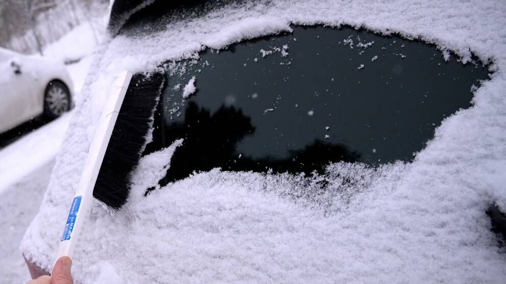 En person sopar snö från bilen.
