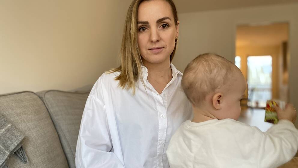 Mamma Micaela Gyllerström har sin dotter i knät. Hon har på sig en vit skjorta och sitter på en ljus soffa, bakgrunden är suddig. Dotter tittar bort från kameran.