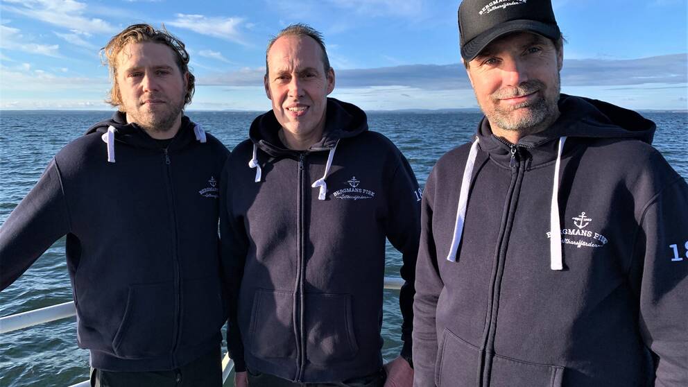 Tre män med blått hav i bakgrunden.