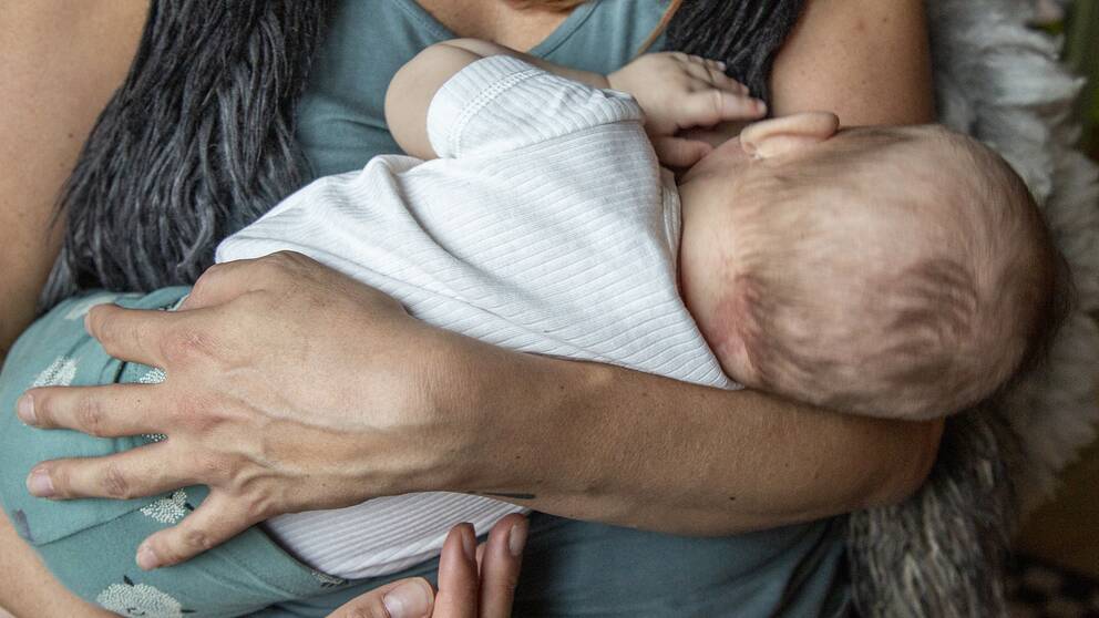 närbild på kvinna som håller ett spädbarn och ammar, ansiktena syns inte