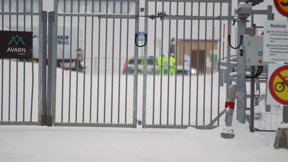 Bakom en stängd grind anas en polisbil och två personer i varselkläder.