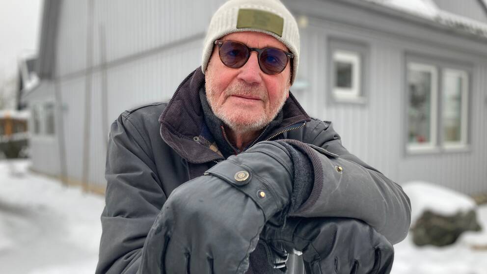 Bilden föreställer Lennart Almqvist, en man i övre medelåldern. Han tittar i in i kameran, han har solglasögon och ljus mössa på huvudet. Han vilar armarna på skaftet till en snöskyffel. I bakgrunden syns hans grå villa. Det är snö ute. 