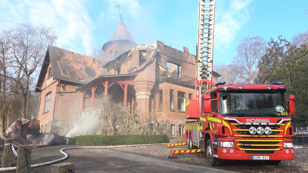 Bilden visar Kockenhus herrgård som totalförstörts i en brand. Taket är svart och det ryker om huset.