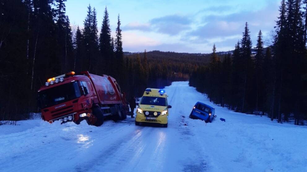 En röd last bil och en blå postbil ligger i diket på varsin del av en snöig väg. Mellan dem står en ambulans.
