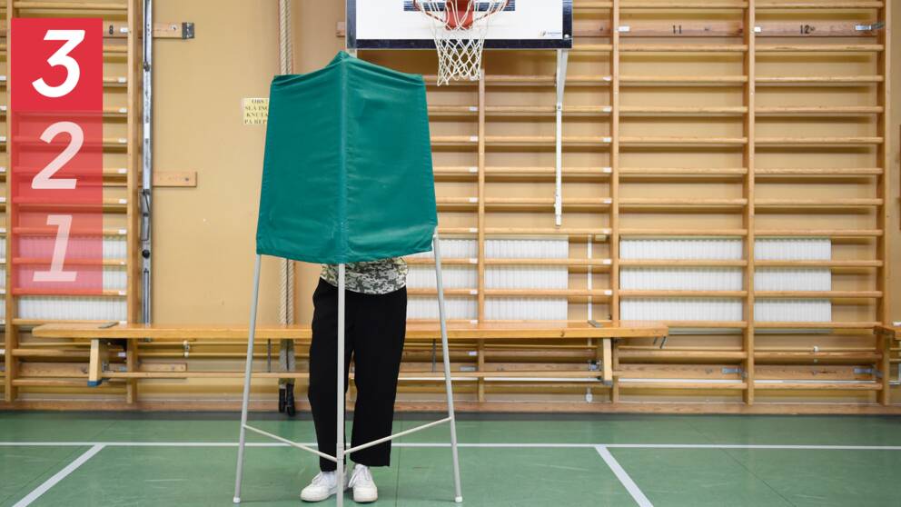 Bild från en vallokal (gymnastikhall). En person står bakom ett grönt valbås