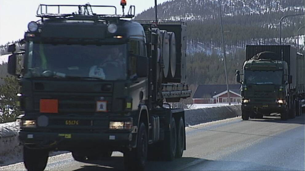 militär-lastbilar på väg, berg med skog och snö på marken i bakgrunden
