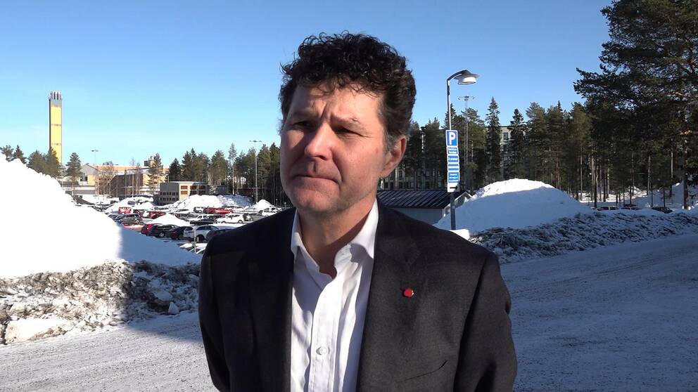 En kostymklädd man står utomhus och kisar.