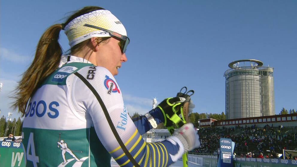 Bild på kvinnlig skidåkare i vit svensk landslagsdress med tornet Arctura i bakgrunden. Från Östersunds skidstadion.