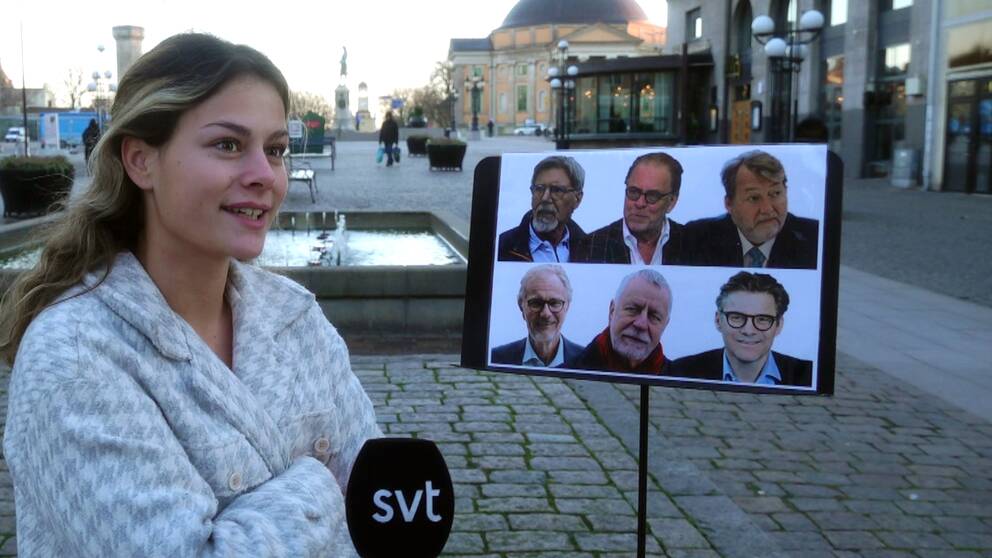 En kvinna står utomhus framför ett plakat som innehåller sex bilder på olika män.