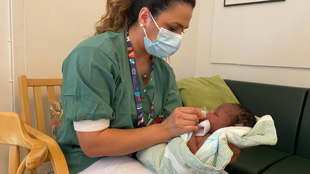 Undersköterskan Avin Saleh sitter i en stol och koppmatar den nyfödda bebisen Uminathi Blose. Bilden är tagen på förlossningskliniken i Eskilstuna.