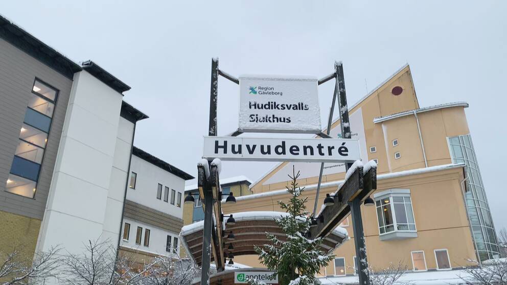 skyltar vid entrén till Hudiksvalls sjukhus, vintertid, snö. Byggnaden i bakgrunden