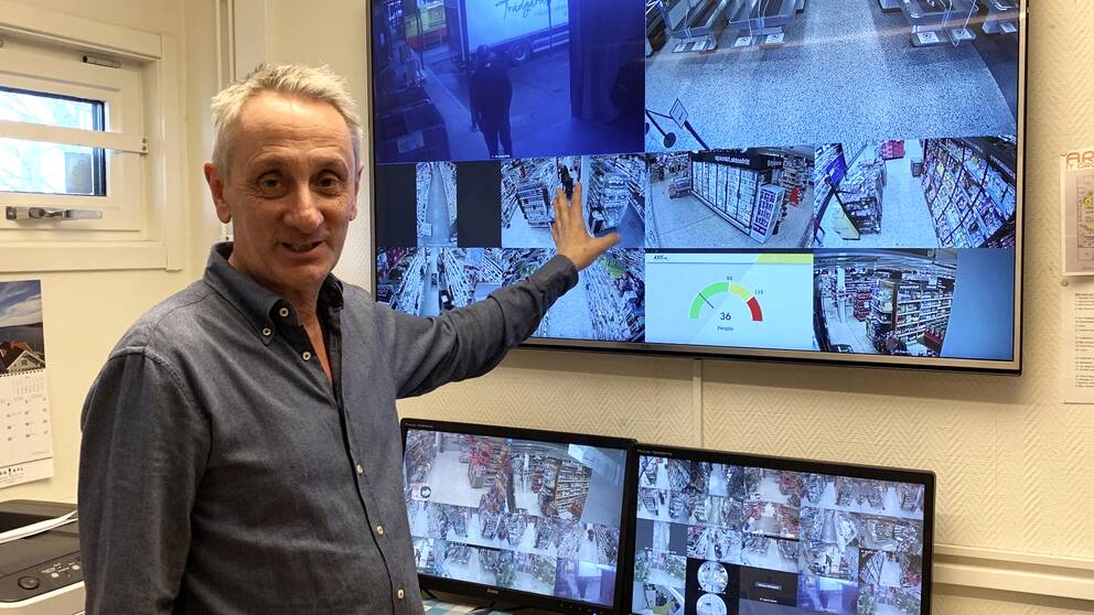 En man står framför ett par skärmar och visar sin kameraövervvakning i en butik.