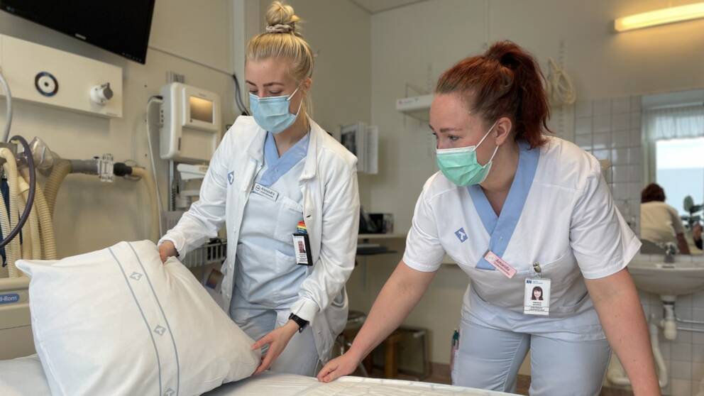Två undersköterskor med munskydd bäddar en säng i en förlossningssal.