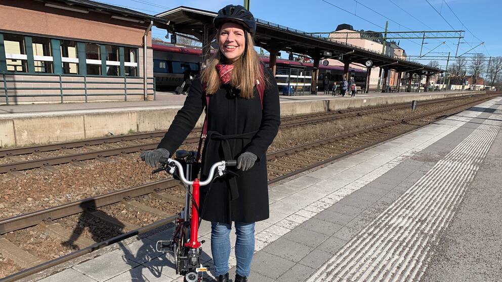 En kvinna som står med en vikbar cykel på en tågstation.