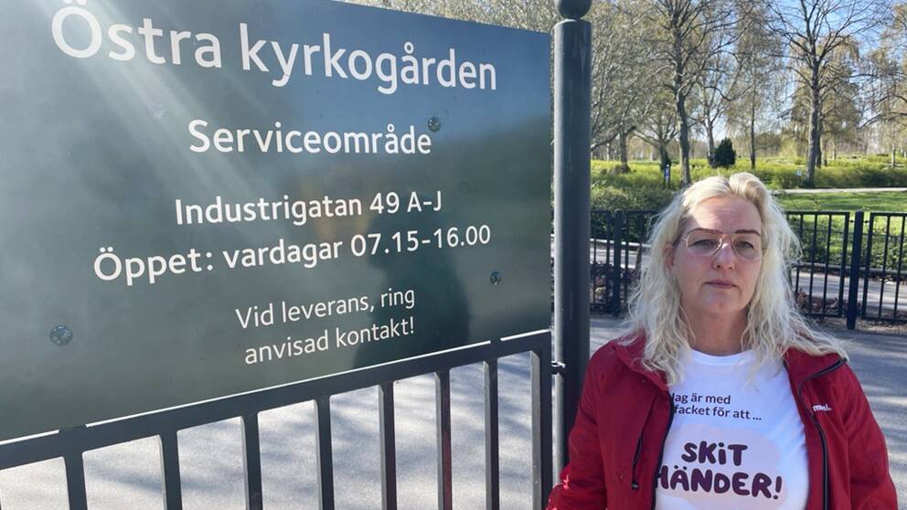 En blond kvinna står intill en skylt vid en kyrkogård.