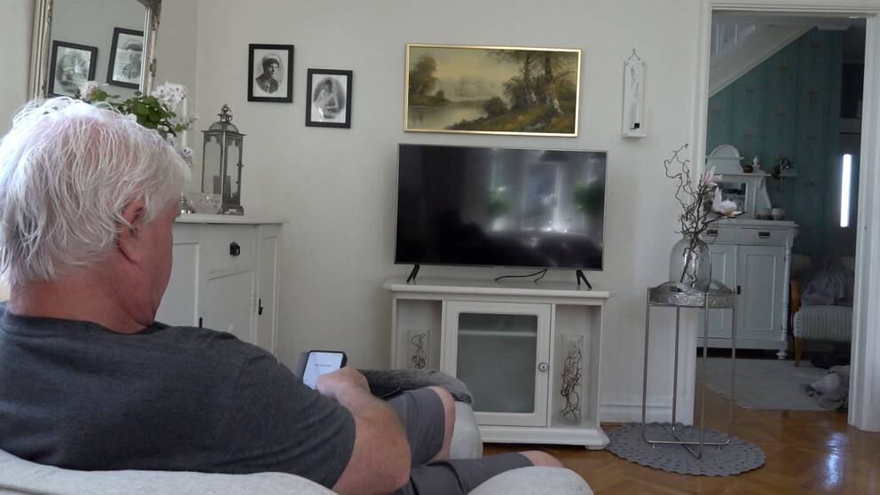 Man sitter i fåtölj framför tv.