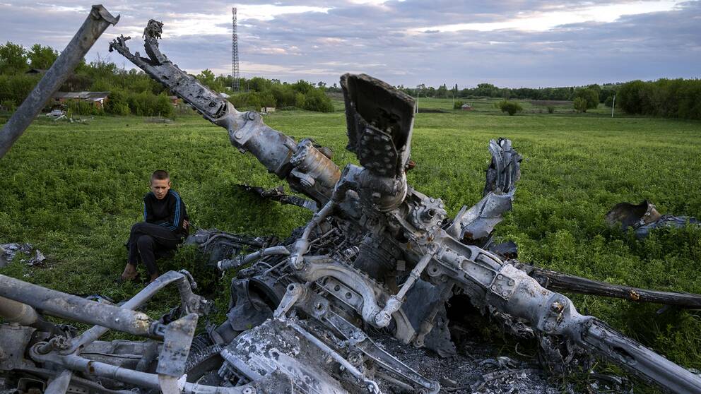 En pojke sitter bredvid skrotet efter en förstörd rysk helikopter i Malaya Rohan i Charkivregionen i Ukraina.