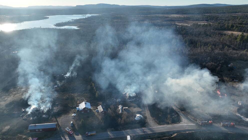 Flygbild över ett område. Mycket rök och flera hus som brinner.