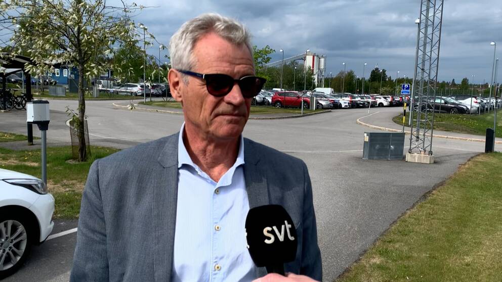 Ulf Holst, i förd skjorta och kavaj och ett par svarta solglasögon, står mitt i bild och en reporter sträcker fram en mikrofon till honom.