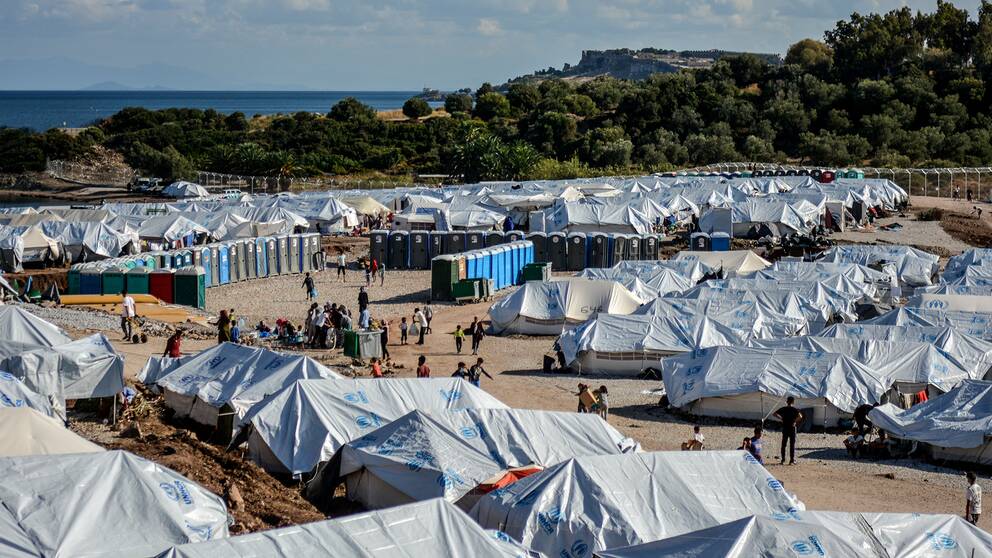 Tiotals vita tält och utomhustoaletter på en stor grusplan på den grekiska ön Lesbos.