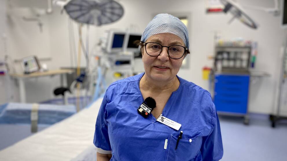 En kvinna med hårnät och blå sjukhuskläder står i en vit operationssal