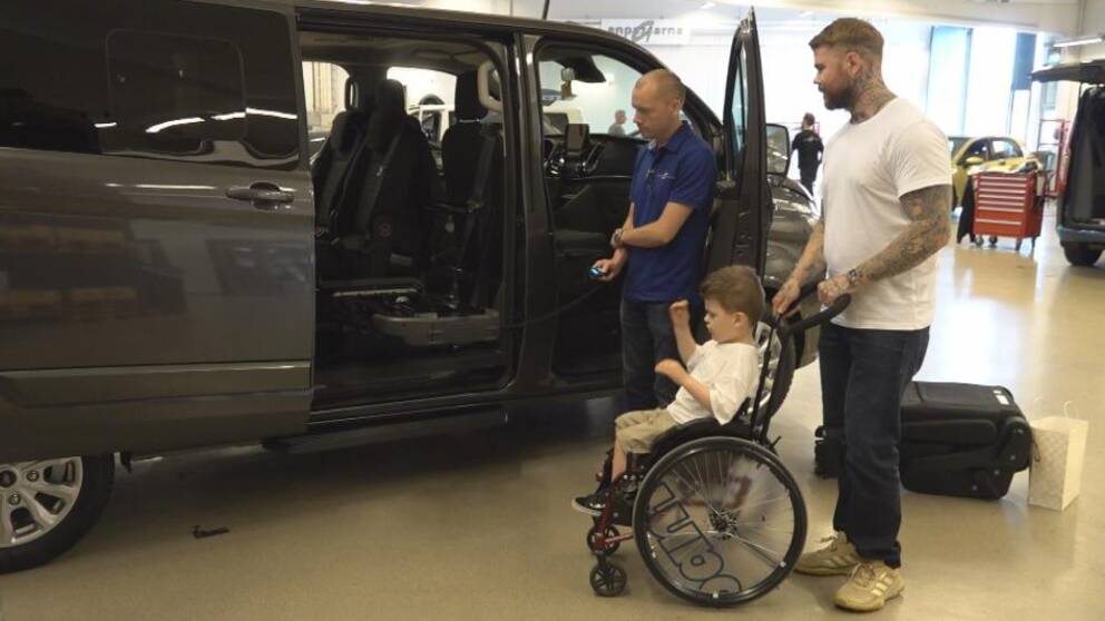 en lite pojke i rullstol, hans pappa, och en man från bilverkstaden tittar på en minibuss med öppen sidodörr