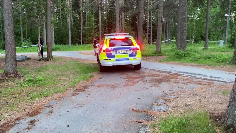 polisbil på cykelväg i skogsområde, tejp-avspärrningar och polismän skymtar längre bort