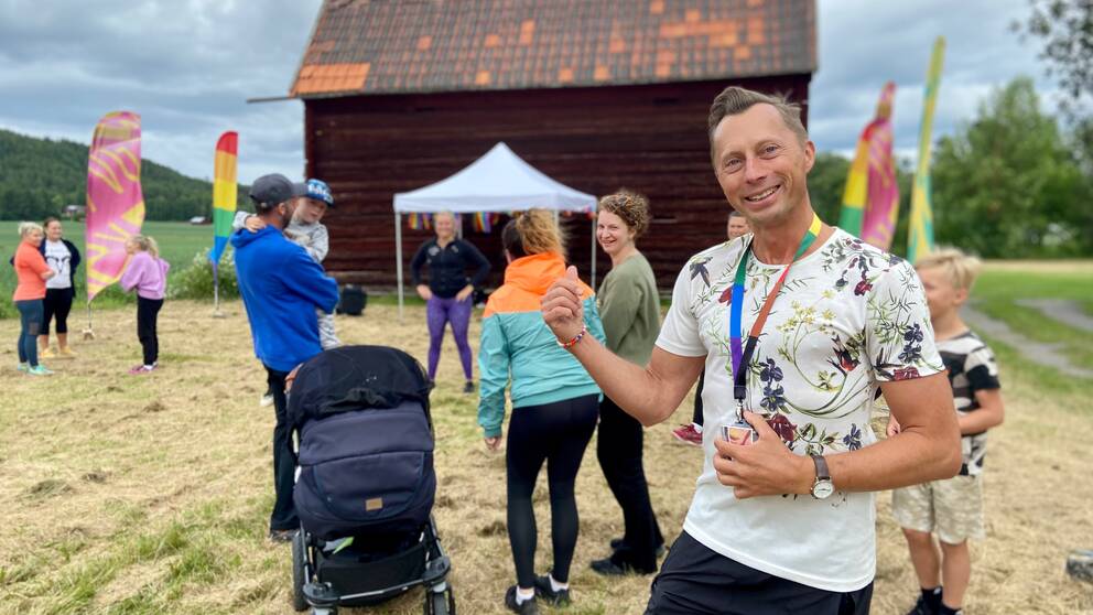 Man med blommig tröja som pekar på ett Pridefirande bakom.